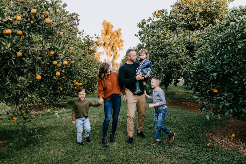 Family Photographer, Family of five walks through an orange grove holding hands